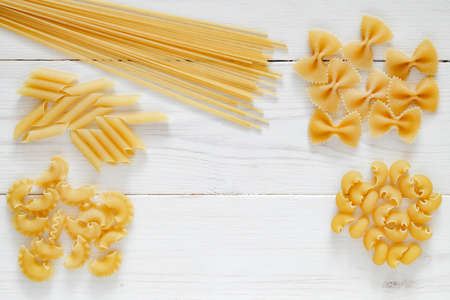 Pasta, set of raw farfalle, spaghetti, pipe, maccheroni, penne, cresta,  on white wooden board background, top view, space to copy text.の写真素材