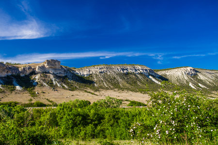 Rocky ledges, cuesta in hilly terrain, white flowers, landscape on clear day