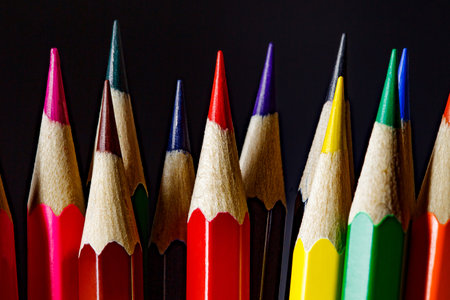 Colored pencils with facets gathered in bundle, sharpened on dark background close-up, selective...