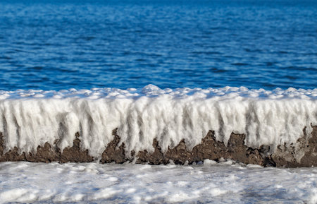 Ice crust from frozen water on concrete parapet on embankment near the seaの写真素材
