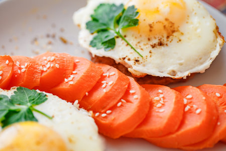 Fried eggs with meat cutlets and carrots with spices and sesame seeds close-up selective focusの写真素材