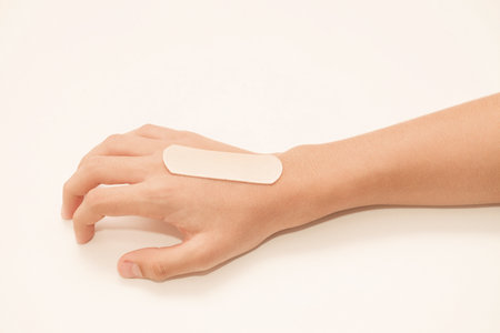Medical adhesive plaster is pasted on hand of child hand, selective focus, on white backgroundの写真素材
