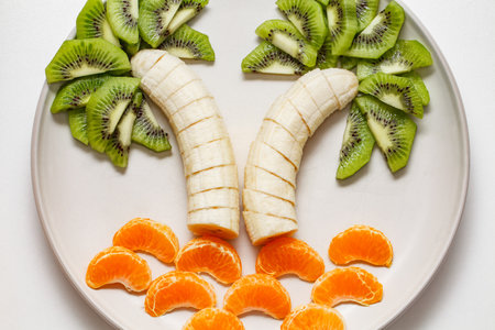 Creative tropical fruit display - palm trees from sliced bananas and kiwi, sea waves from slice of tangerinesの写真素材