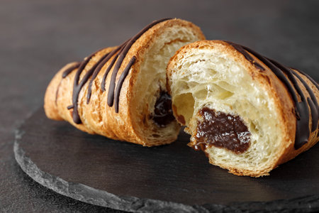 Croissant cut in half with chocolate filling inside, on slate stone plate round, dark background, selective focusの写真素材