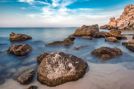Stones in water and rocks on seashore, blurred water movementの写真素材