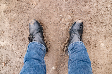 men's feet in jeans and boots standing in the mud, top view
