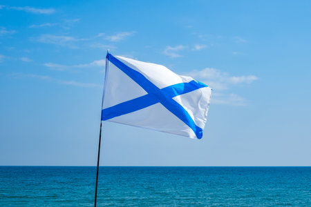 symbol of military fleet flies white flag with blue cross on wind against sky and seaの写真素材