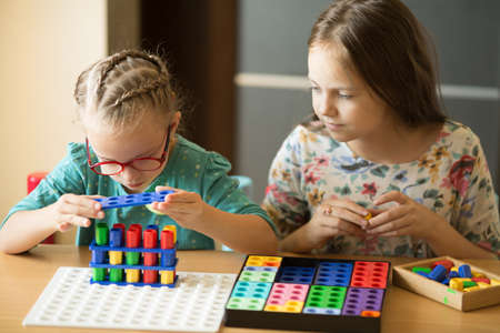 A girl with Down syndrome is engaged in elementary mathematics with her older sister, having fun playingの写真素材