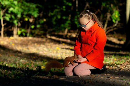 A girl with down syndrome feeds a squirrel nuts in the forest at sunsetの写真素材