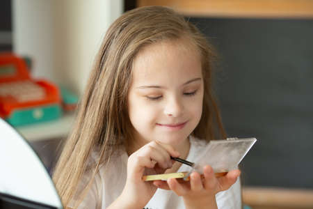 Beautiful girl with Down syndrome combing her hair in front of a mirror at homeの写真素材