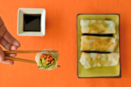 Summer rolls filled with raw vegetables with a container of soy sauce. Closeup on an opened summer...