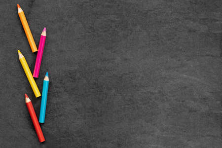 Colored pencils are laid out on a school black board, layout.の写真素材