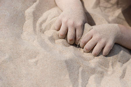 Sand dunes close-up with areas of sharpness and defocus, children's hands squeeze the sandの写真素材