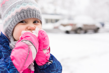 Cute little bundled up girl eating snow outsideの写真素材