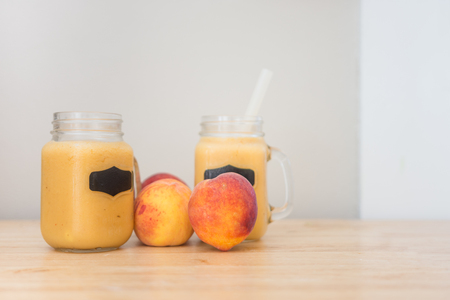 Glass jars with handles full of fresh peach puree next to large fresh peachesの写真素材