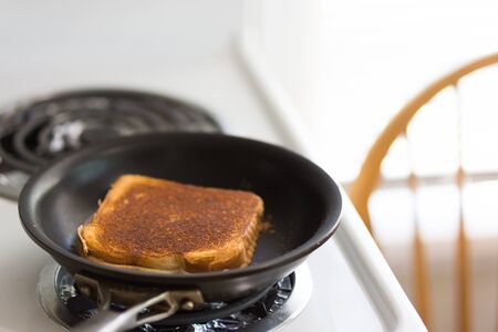 Golden brown grilled cheese cooking in black frying pan on stove topの写真素材