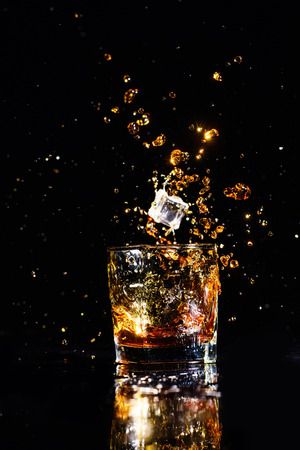 Isolated shot of whiskey with splash on black background, brandy in a glassの写真素材