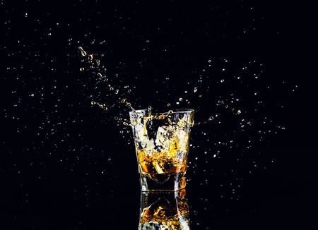 Isolated shot of whiskey with splash on black background, brandy in a glassの写真素材