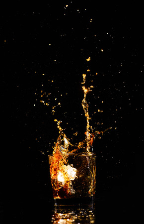 Isolated shot of whiskey with splash on black background, brandy in a glassの写真素材