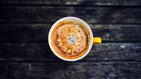 A yellow cup of tasty coffee, on rustic wooden table backgroundの写真素材