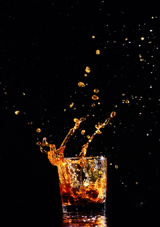 Isolated shot of whiskey with splash on black background, brandy in a glassの写真素材