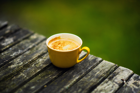 A yellow cup of tasty coffee, on rustic wooden table backgroundの写真素材