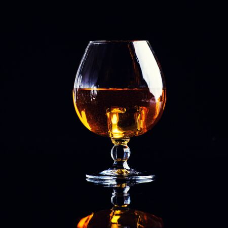 glass with cognac with splash on a black background