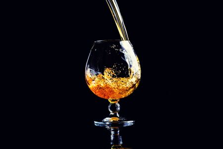 glass with cognac with splash on a black backgroundの写真素材