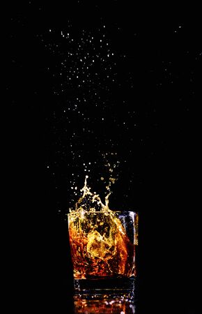 Isolated shot of whiskey with splash on black background, brandy in a glassの写真素材