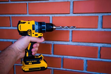 cordless drill and a drill in the hands of man against the background of a brick wallの写真素材