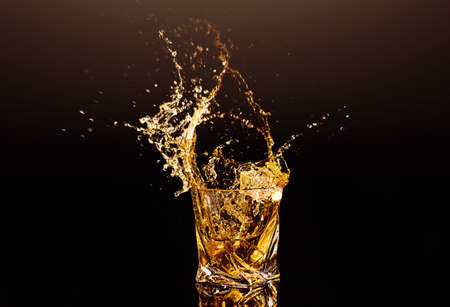 A glass of whiskey with splashes from the ice cube over black background. alcohol splashes. whiskey or cognac or another type of alcoholの写真素材