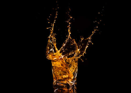 A glass of whiskey with splashes from the ice cube over black background. alcohol splashes. whiskey or cognac or another type of alcoholの写真素材