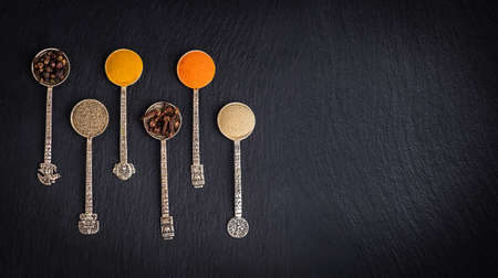 Various herbs and spices on black stone plate. Black pepper, turmeric, ginger, saffron, cloves.の写真素材