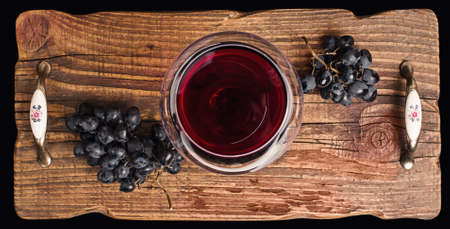Red wine in a glass and ripe grapes on rustic textured wooden tray.の写真素材