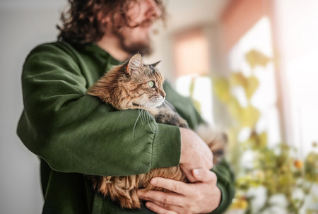 Man hugging a cat by the window with flowerpots.の写真素材