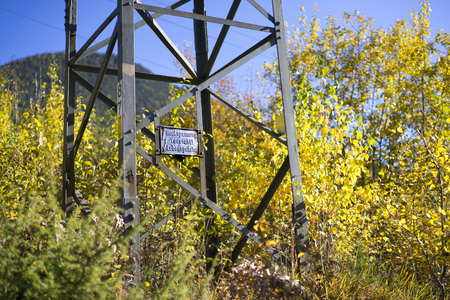 Detail of Hydro Electric Tower Support with Sign Amongst Lush Forest Vegetation on Sunny Day with Clear Blue Sky in Alpine Region, Tyrol, Austriaの写真素材