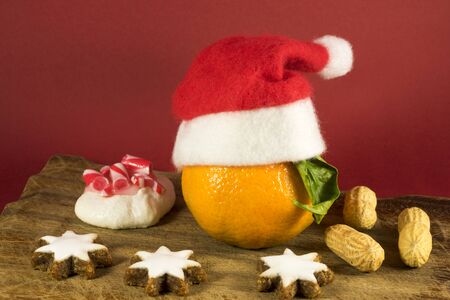 Colorful Christmas still life decoration with star shaped cookies, nuts, meringue and a festive clementine with a red Santa Hatの写真素材
