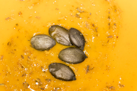 Dried pumpkin pips and scattered spices on pumpkin soup in a close up full frame background viewの写真素材