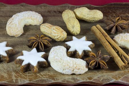 Christmas cookie and spice background with iced star and crescent shapes vanilla cookies, peanuts, star anise and stick cinnamon on an old wooden chopping board in a close up low angle viewの写真素材