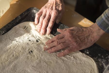 High Angle View Senior woman Hands Stretching and Fitting Raw Thin Crust Dough for Pizza into Rectangular Pan on Sunny Kitchen Counterの写真素材