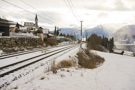 Snow covered railway tracks in a winter landscape passing a small town or village in alpine sceneryの写真素材