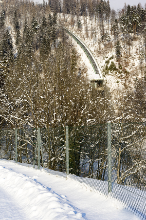 View from road along fence of cable railway tracks with building going up steep snowy hill in winterの写真素材