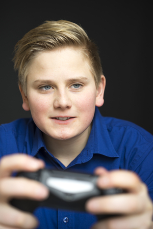 Single intense male youth in blue shirt with grin and blond hair holding a dual joystick video game controllerの写真素材