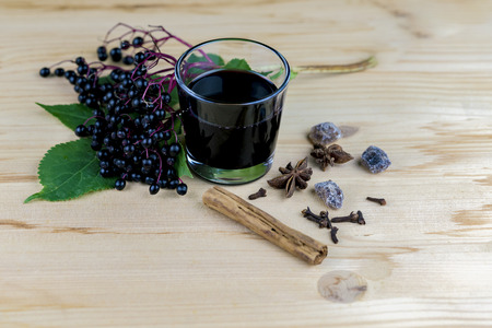 Bunch of fresh elderberries with a glass of liquidised juice and spices on a wooden table with copy spaceの写真素材