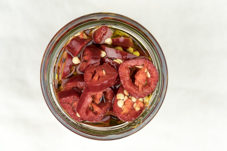 Hot sliced red cayenne chili peppers in olive oil preserved in a glass jar for use as a seasoning and cooking ingredientの写真素材