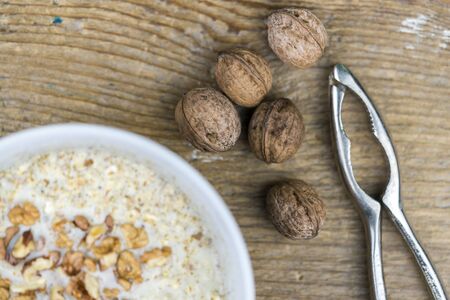 Whole fresh walnuts and a simple metal nutcracker alongside a bowl of cereal topped with chopped...