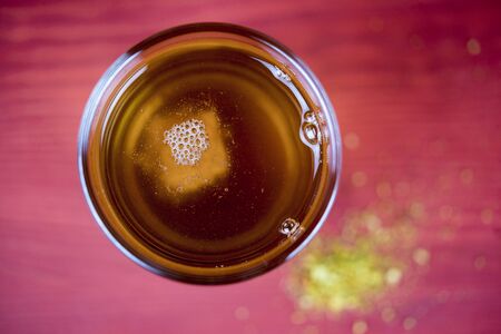 Overhead view of a cup of hot turmeric tea with yellow turmeric powder on a red table below viewed...