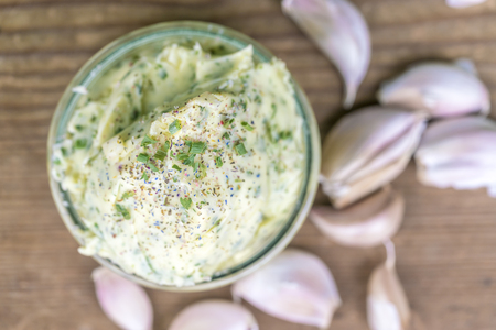 Overhead view of bowl of garlic butter and garlic cloves on wooden tableの写真素材