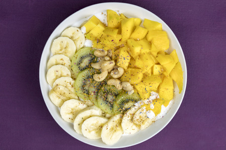 Sliced fresh fruit neatly arranged with healthy cashew nuts on a white plate for a delicious snack over a blue background viewed from aboveの写真素材