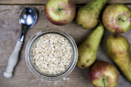 Oatmeal in glass bowl on wooden table with spoon and fruits apples and pears blurred. Close-up from above view - healthy breakfast conceptの写真素材